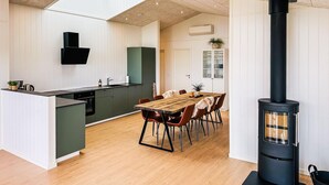 Une cuisine moderne dotée d’un îlot central, d’un coin repas avec une table et des chaises en bois, et d’un poêle à bois noir.