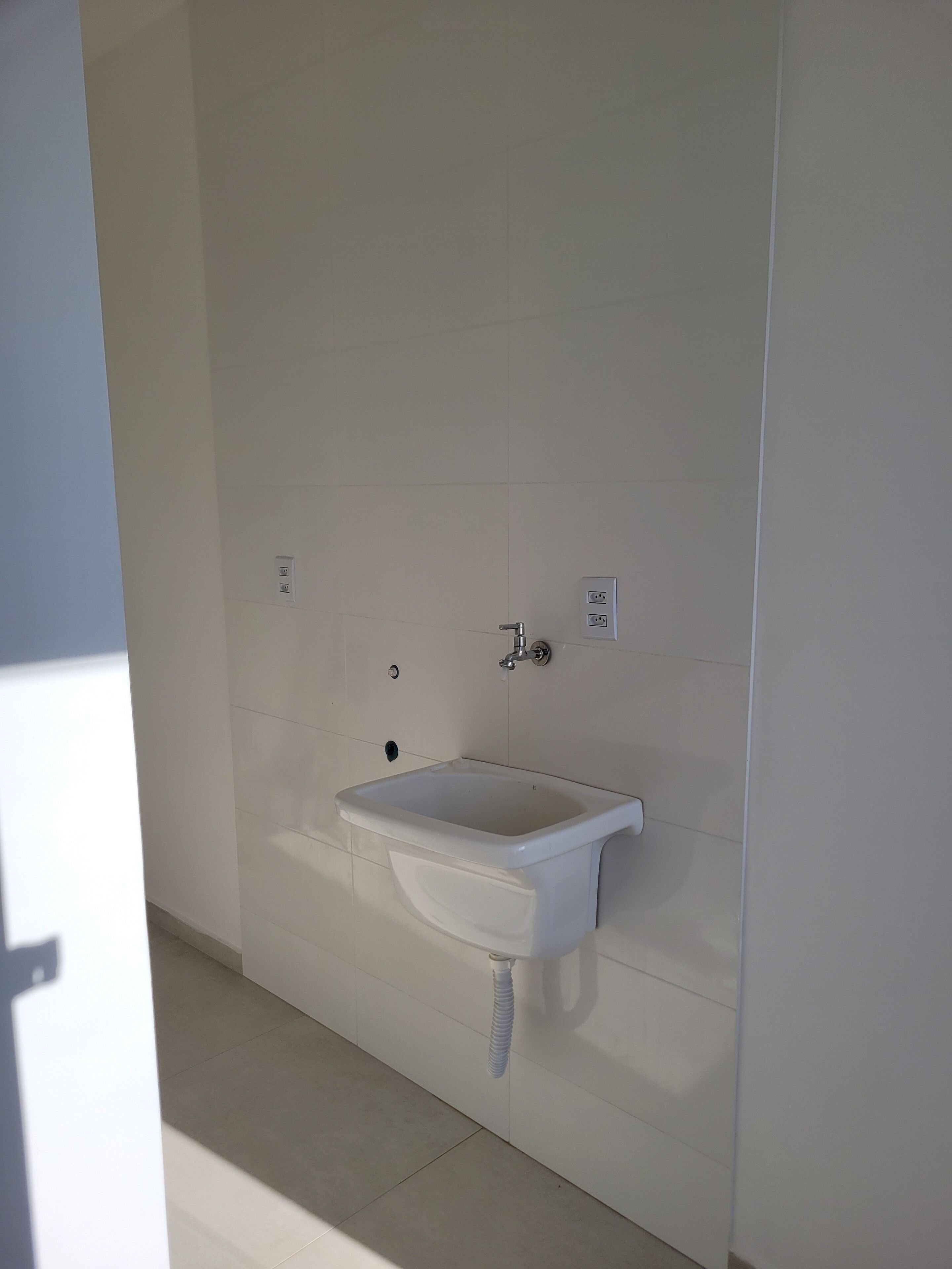 A bathroom with a white sink, a wall-mounted faucet, and a single electrical outlet.
