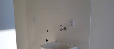 A bathroom with a white sink, a wall-mounted faucet, and a single electrical outlet.