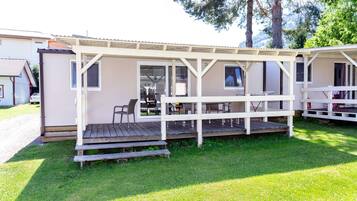 A small, single-story building with a covered patio area, a wooden deck, and a seating arrangement.