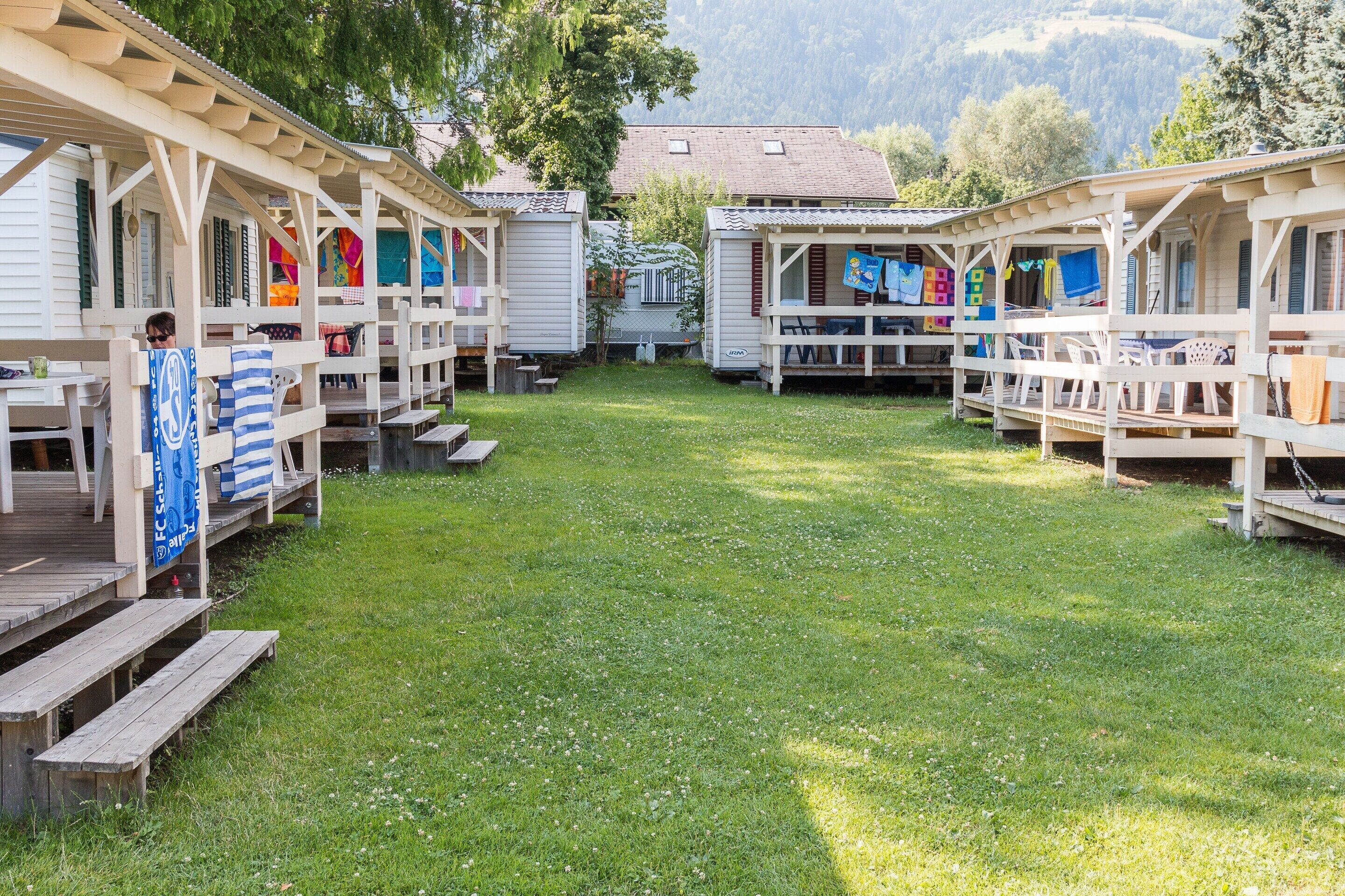 A campground with wooden cabins, each with a porch and a table.