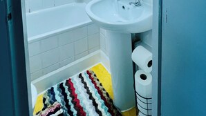A bathroom with a bathtub, a sink, and a mirror. There are shelves with toiletries and a shower curtain.