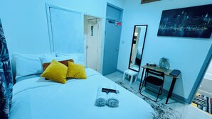 A hotel room with a bed, two pillows, a mirror, a small table with a plant, and a painting on the wall.