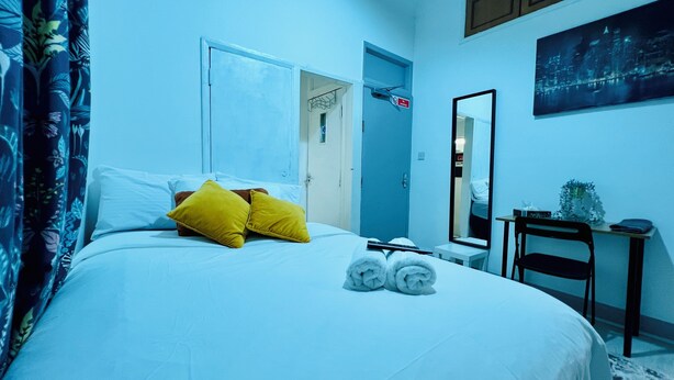 A hotel room with a bed, a desk, a chair, a mirror, and a door.