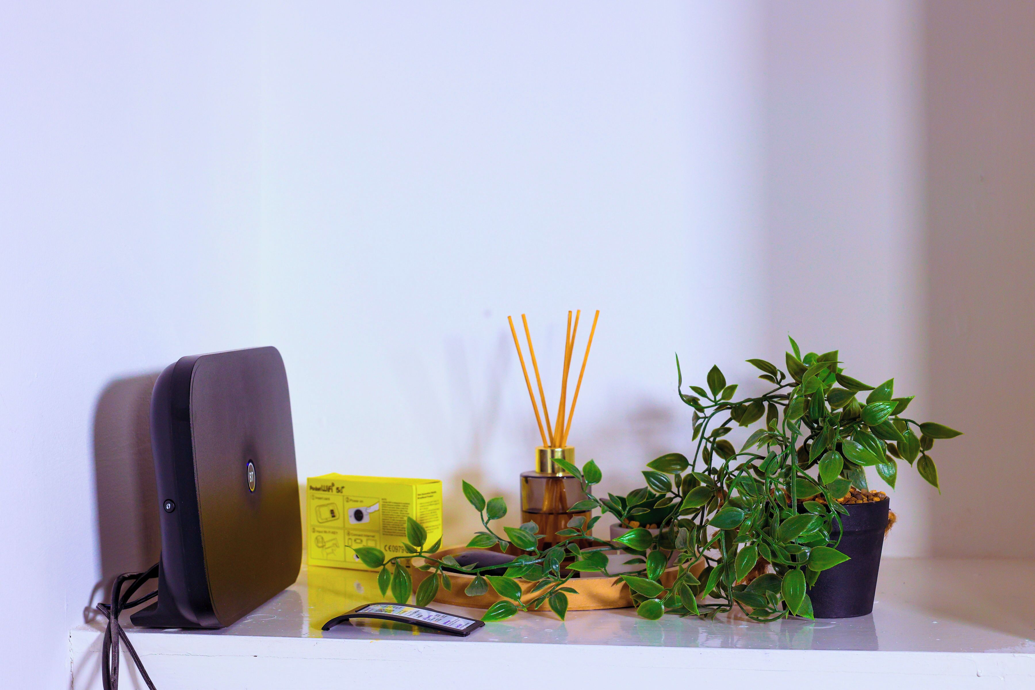 A desk with a laptop, a yellow box, a potted plant, and a reed diffuser.