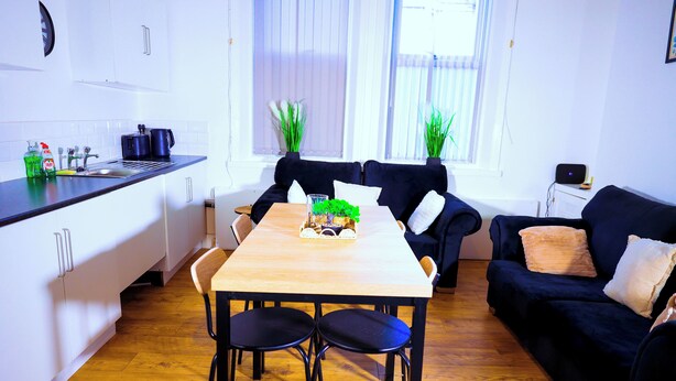 Une cuisine moderne avec des meubles blancs, un plan de travail noir et une table à manger en bois accompagnée de deux chaises.