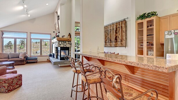 A spacious living room with a fireplace, a kitchen with a bar area, and large windows offering a view of the outdoors. - Snowcreek 811- Beautiful views, Spacious (Mammoth Lakes)