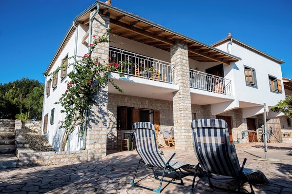 A two-story building with a balcony, stone pillars, and a paved courtyard. - Terra Ionian (Pyrgos)