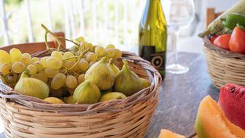 Una cesta de mimbre con uvas e higos, una botella de vino y una copa de vino sobre una mesa.