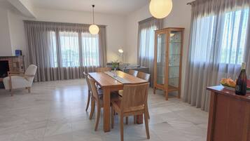Een moderne woonkamer met een eethoek, met een houten tafel, stoelen, een bank en een glazen kast.