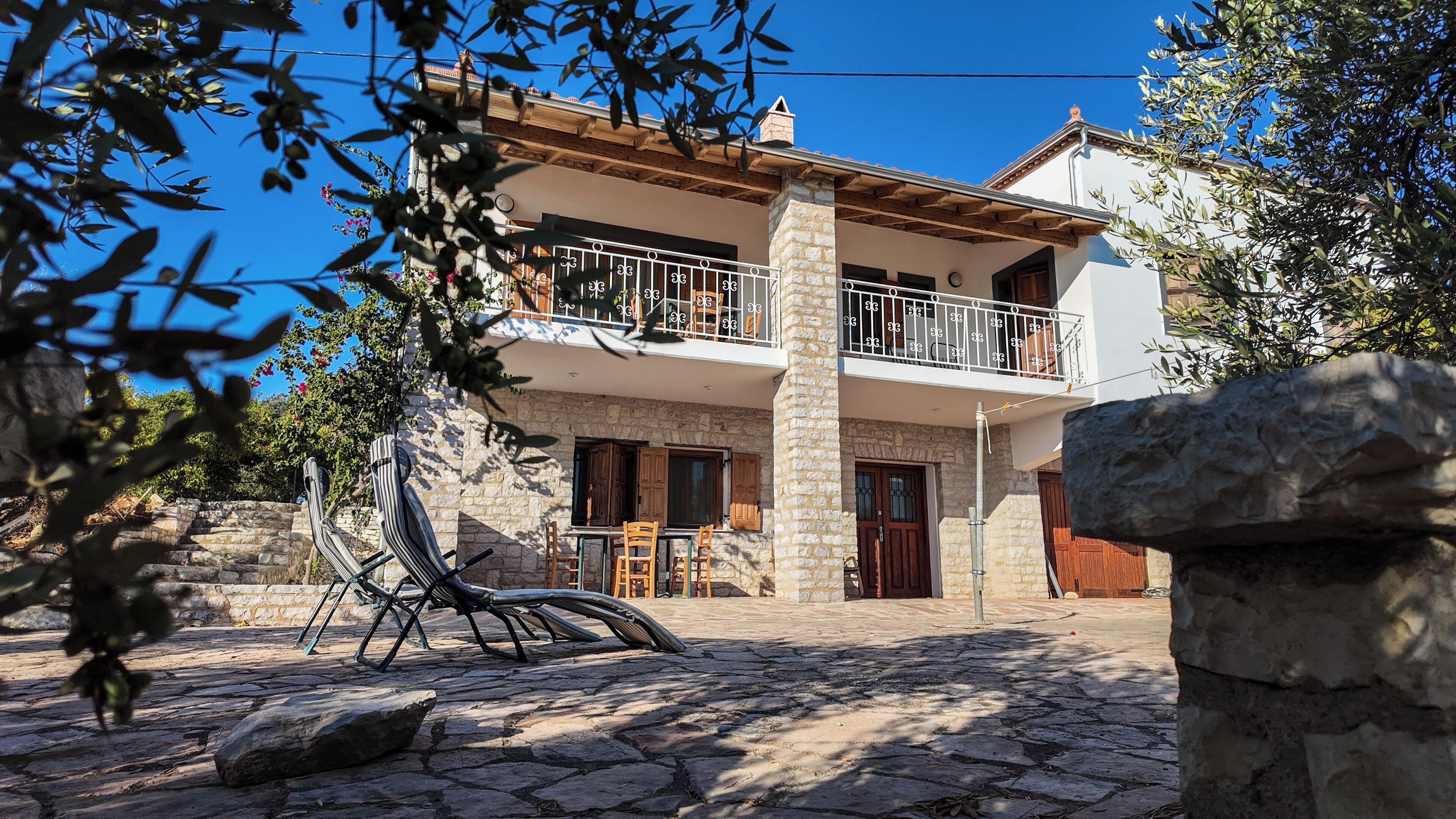 Una casa de piedra de dos pisos con un balcón, escalones de piedra y mobiliario exterior.