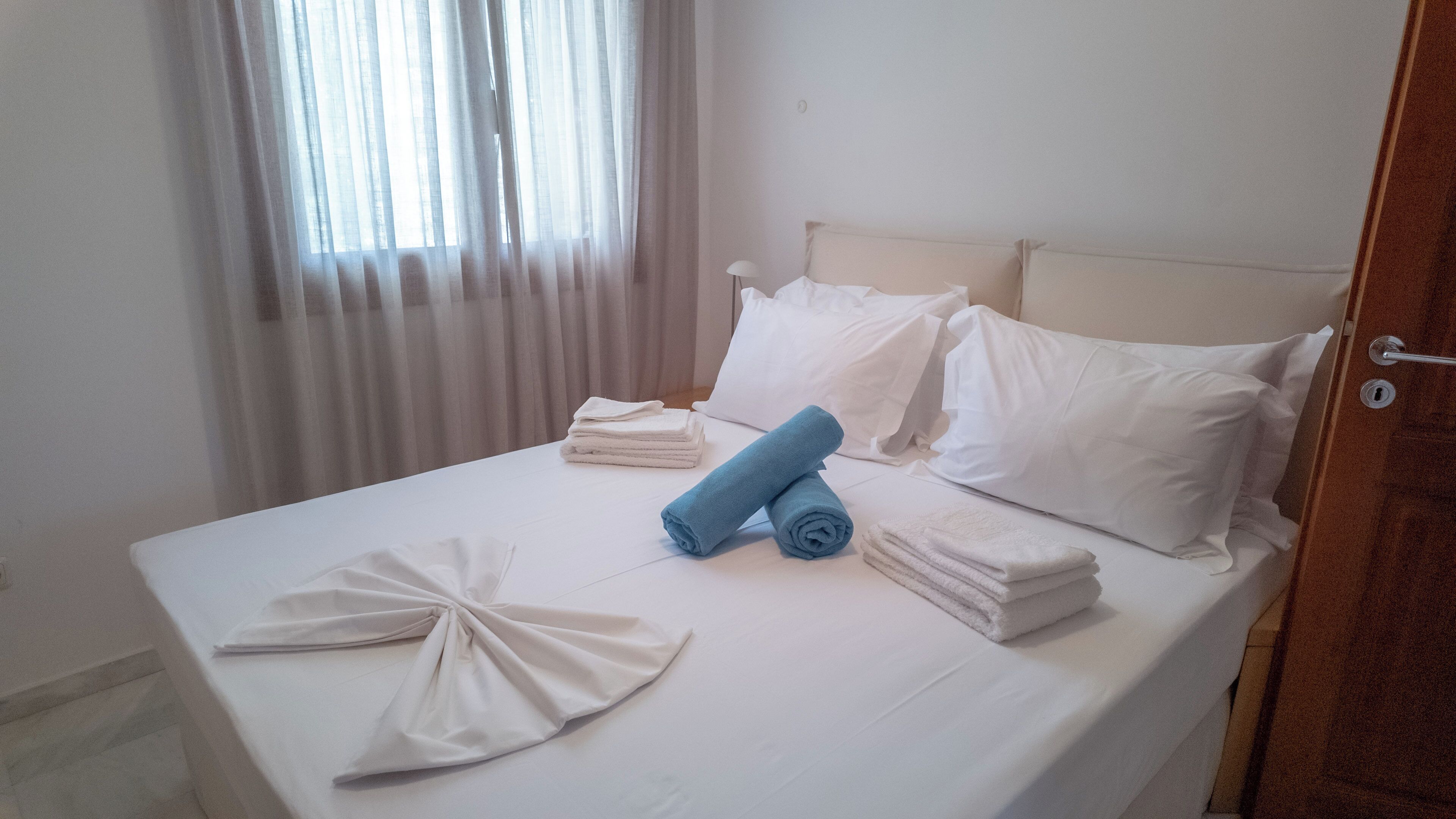 Una cama bien hecha con sábanas blancas, una toalla azul y una toalla blanca doblada.