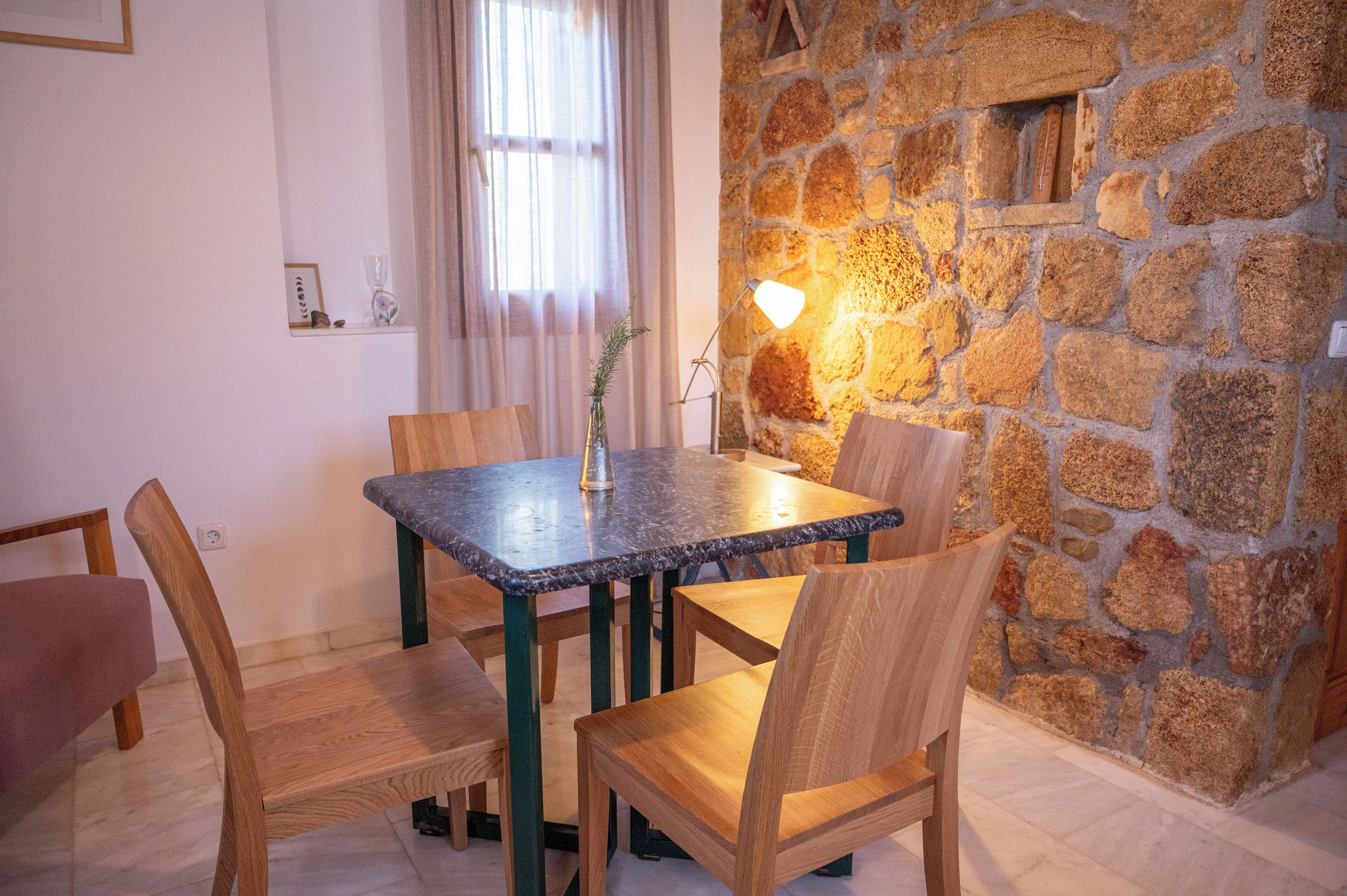 A dining area with a stone wall, a table with chairs, and a vase with a plant.