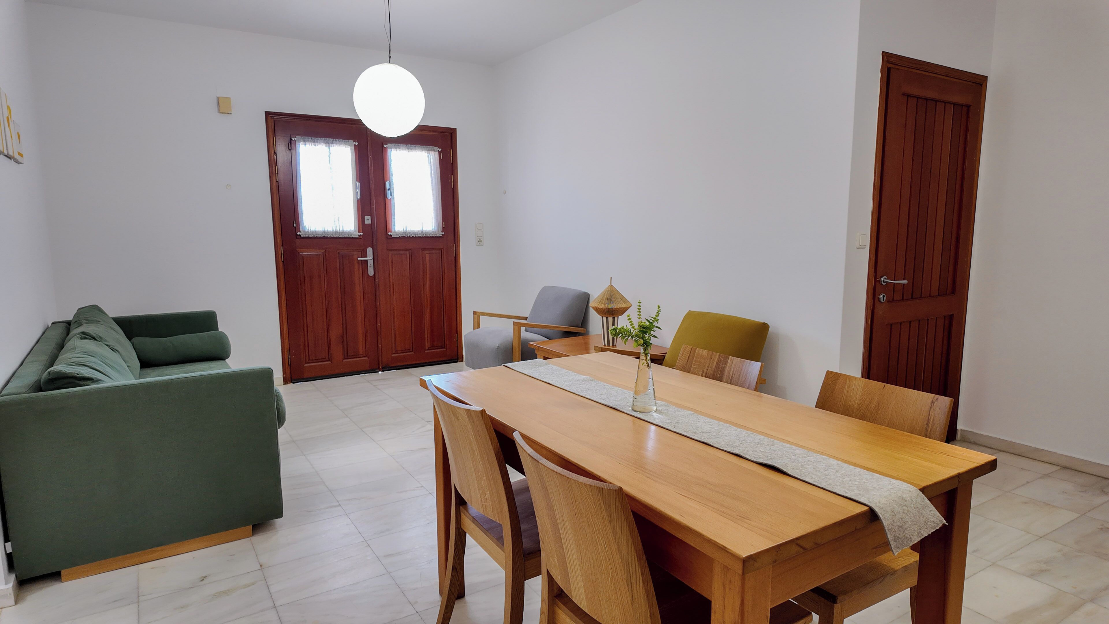A dining area with a wooden table, chairs, a sofa, and a door with a window.