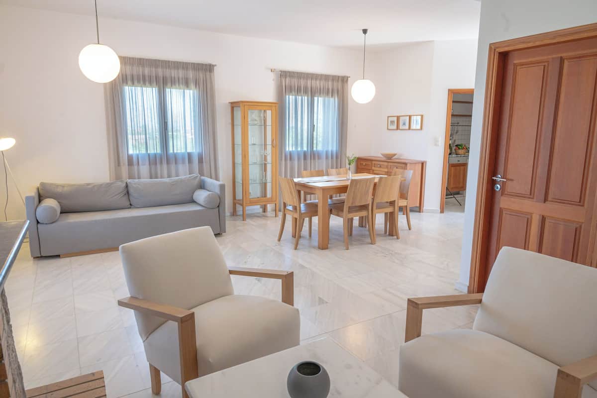 A modern living room with a sofa, two armchairs, a dining table with chairs, and a cabinet.