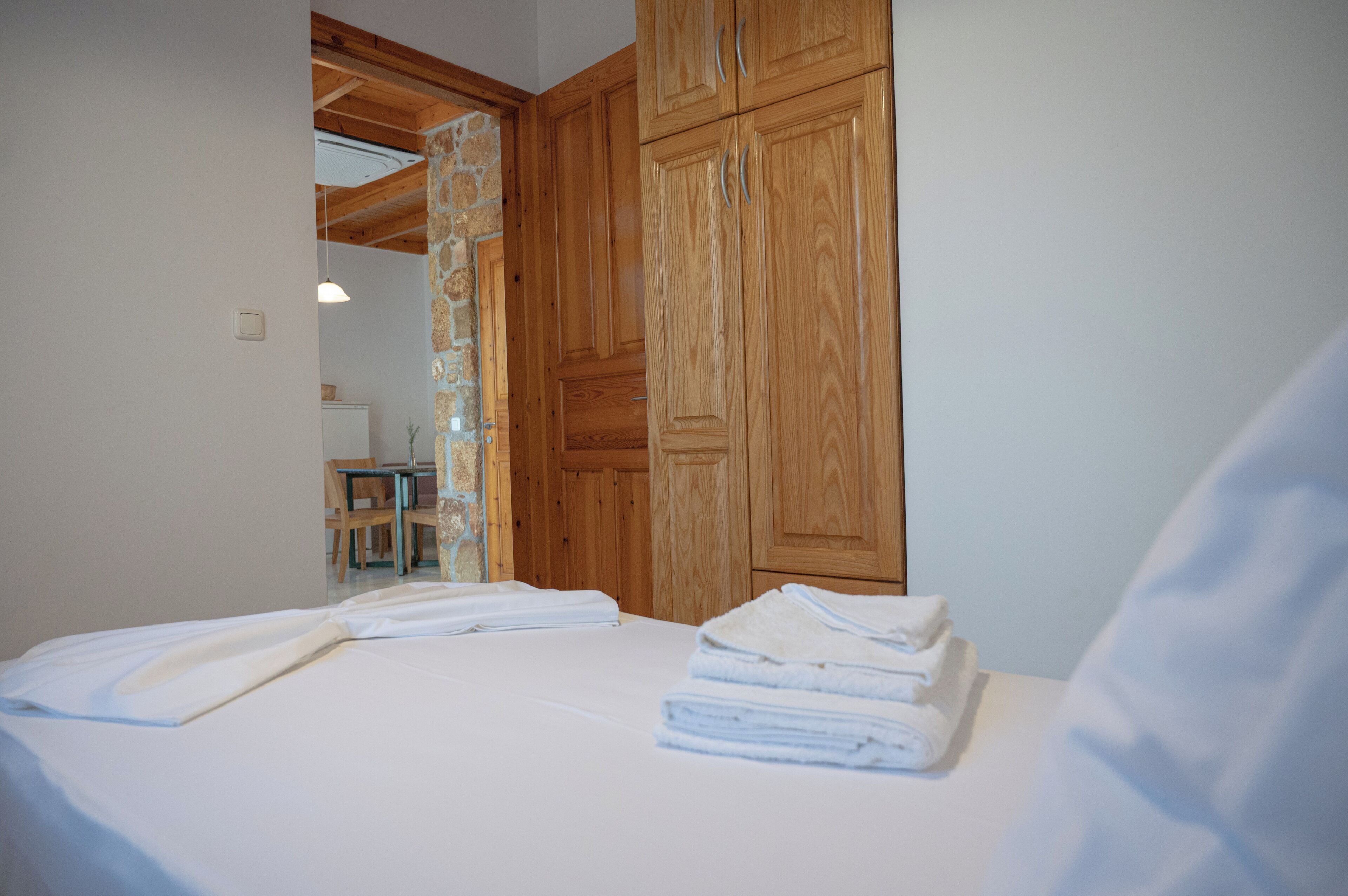 A bedroom with wooden cabinets, a bed with white linens, and a small table with a chair.