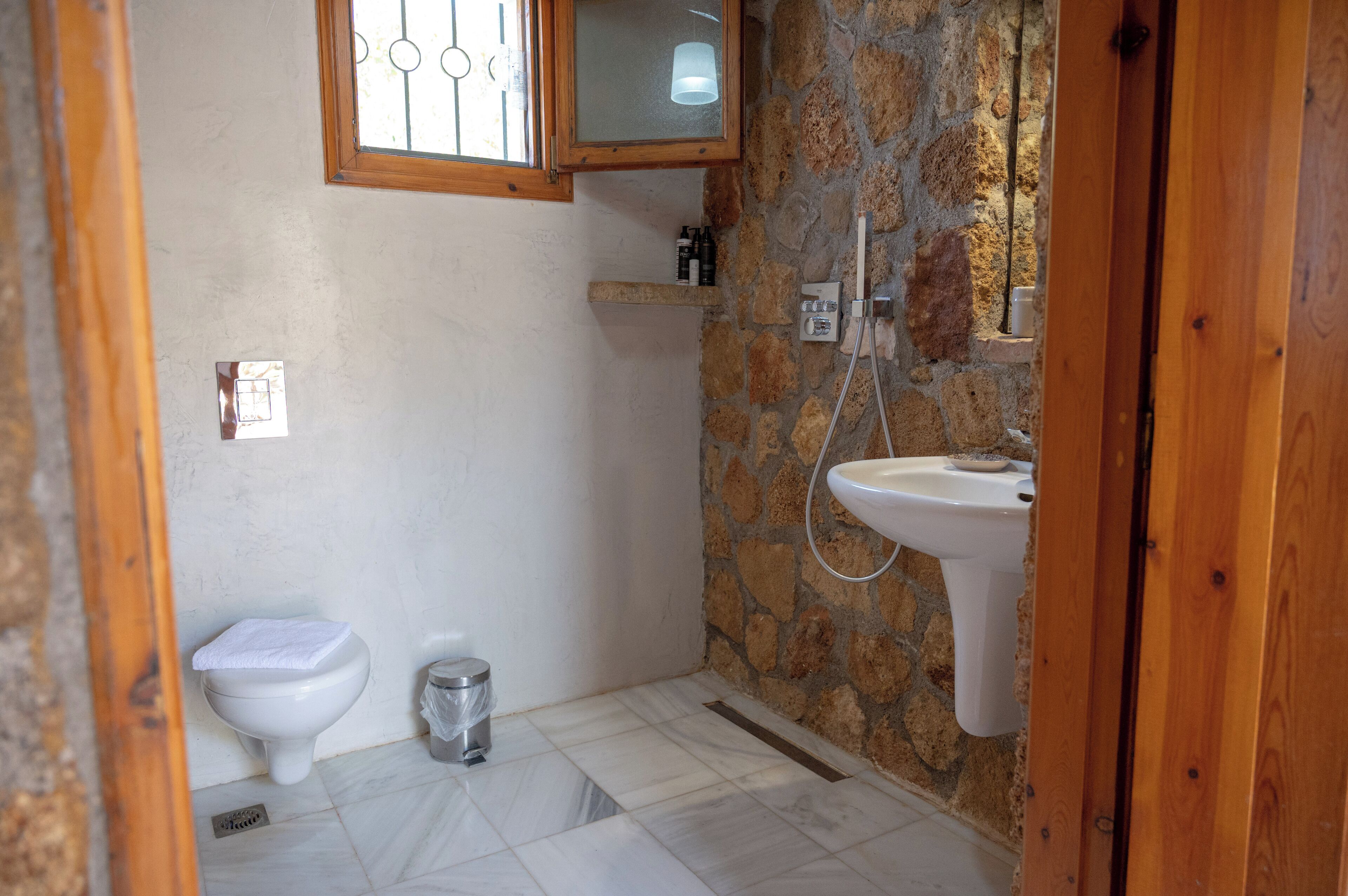 A bathroom with a toilet, a sink, a shower, and a stone wall.