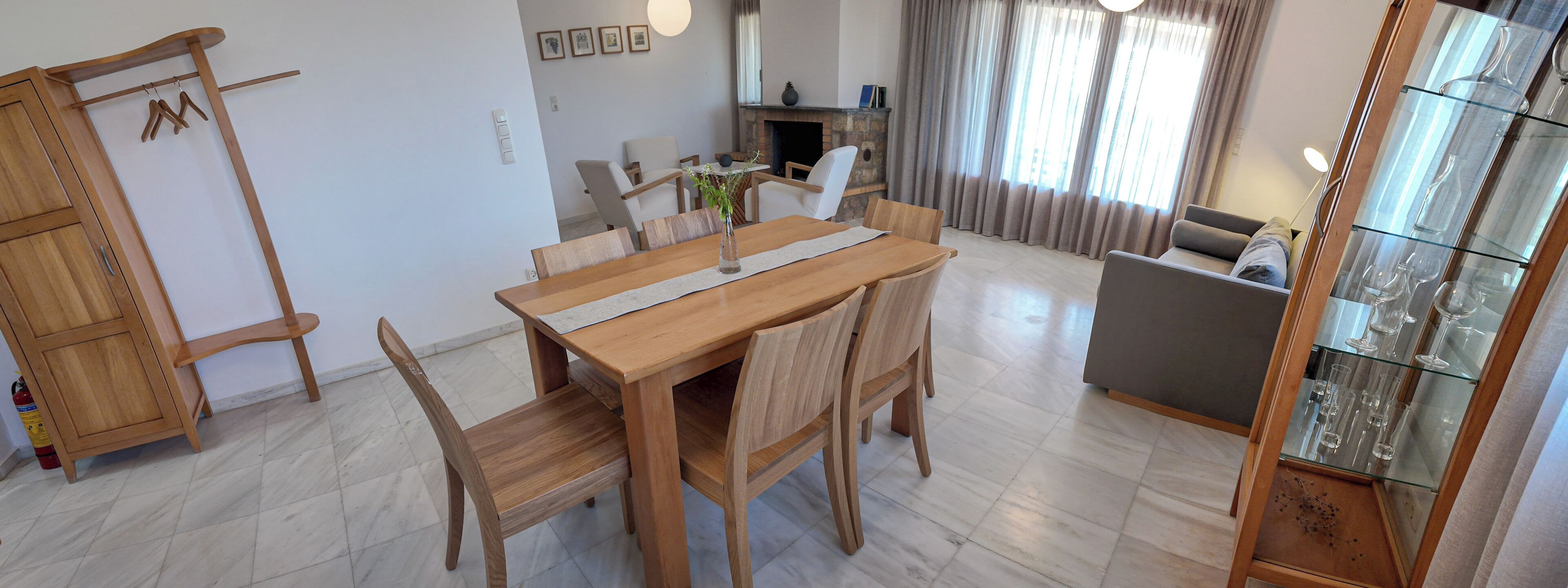 A dining area with a wooden table and chairs, a fireplace, and a glass display case with wine glasses.