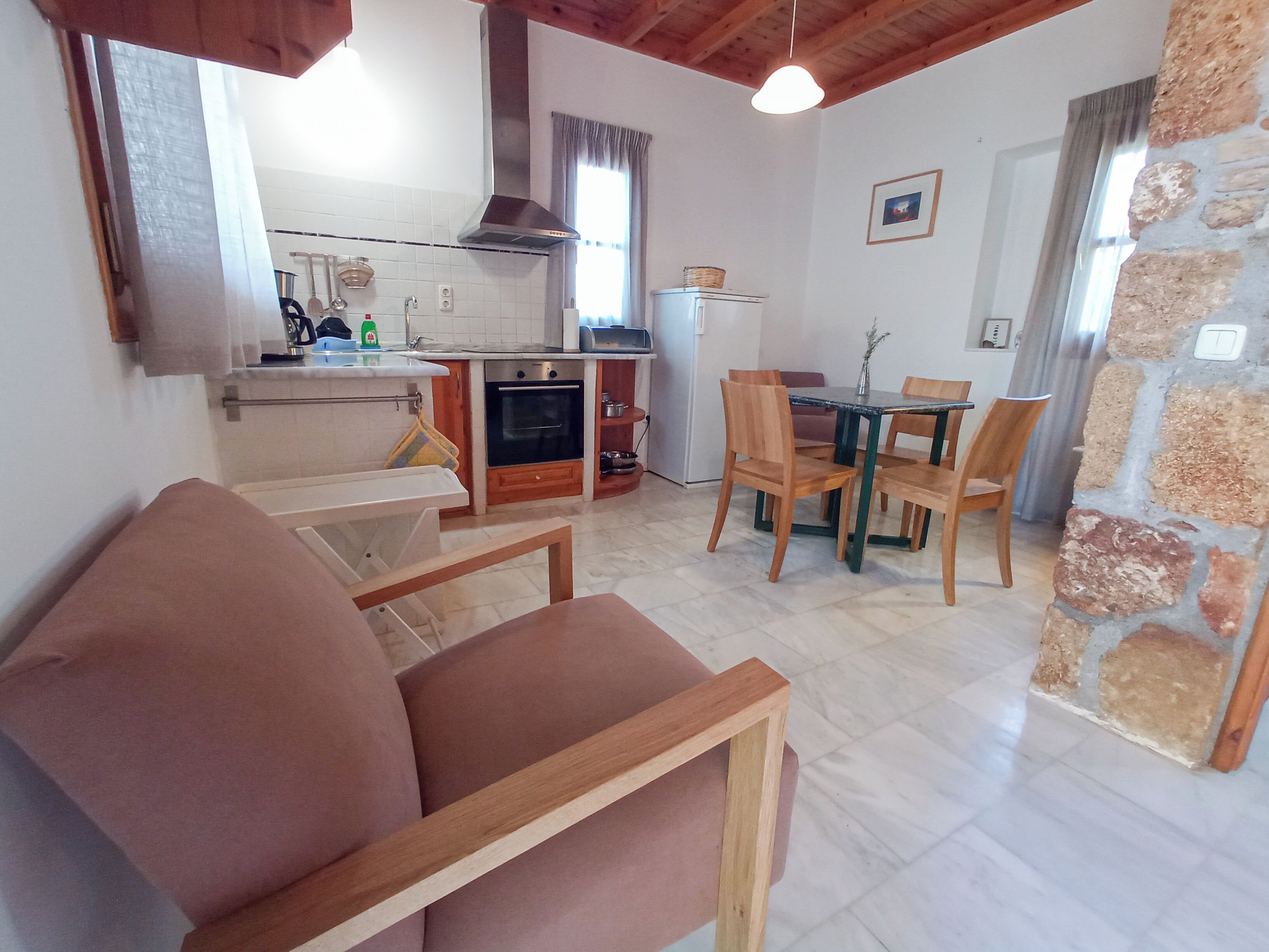 A cozy living room with a sofa, a dining table with chairs, a kitchen area with a stove and oven, and a stone wall.
