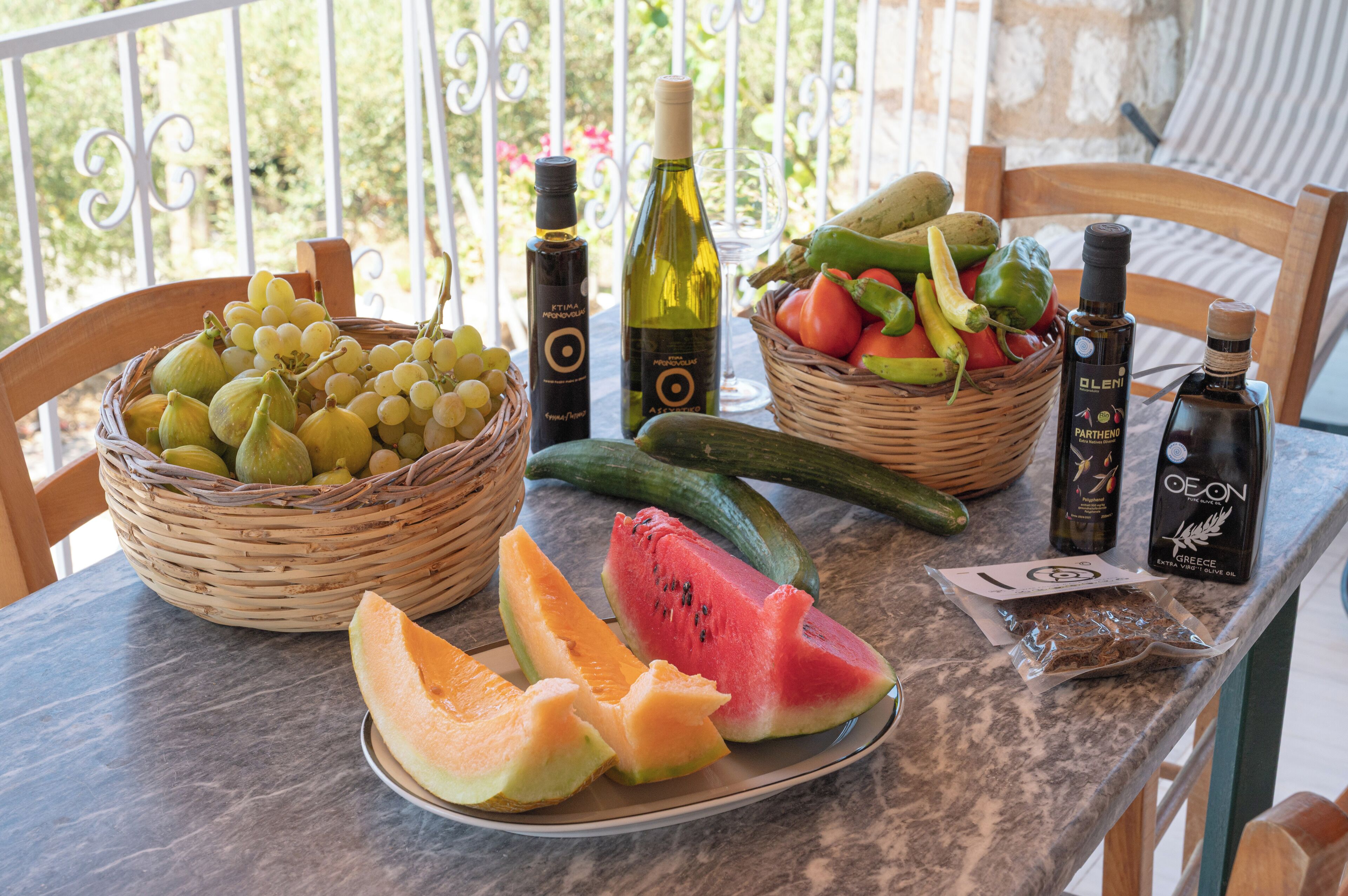Una mesa con frutas variadas, botellas de aceite de oliva y una cesta de uvas.