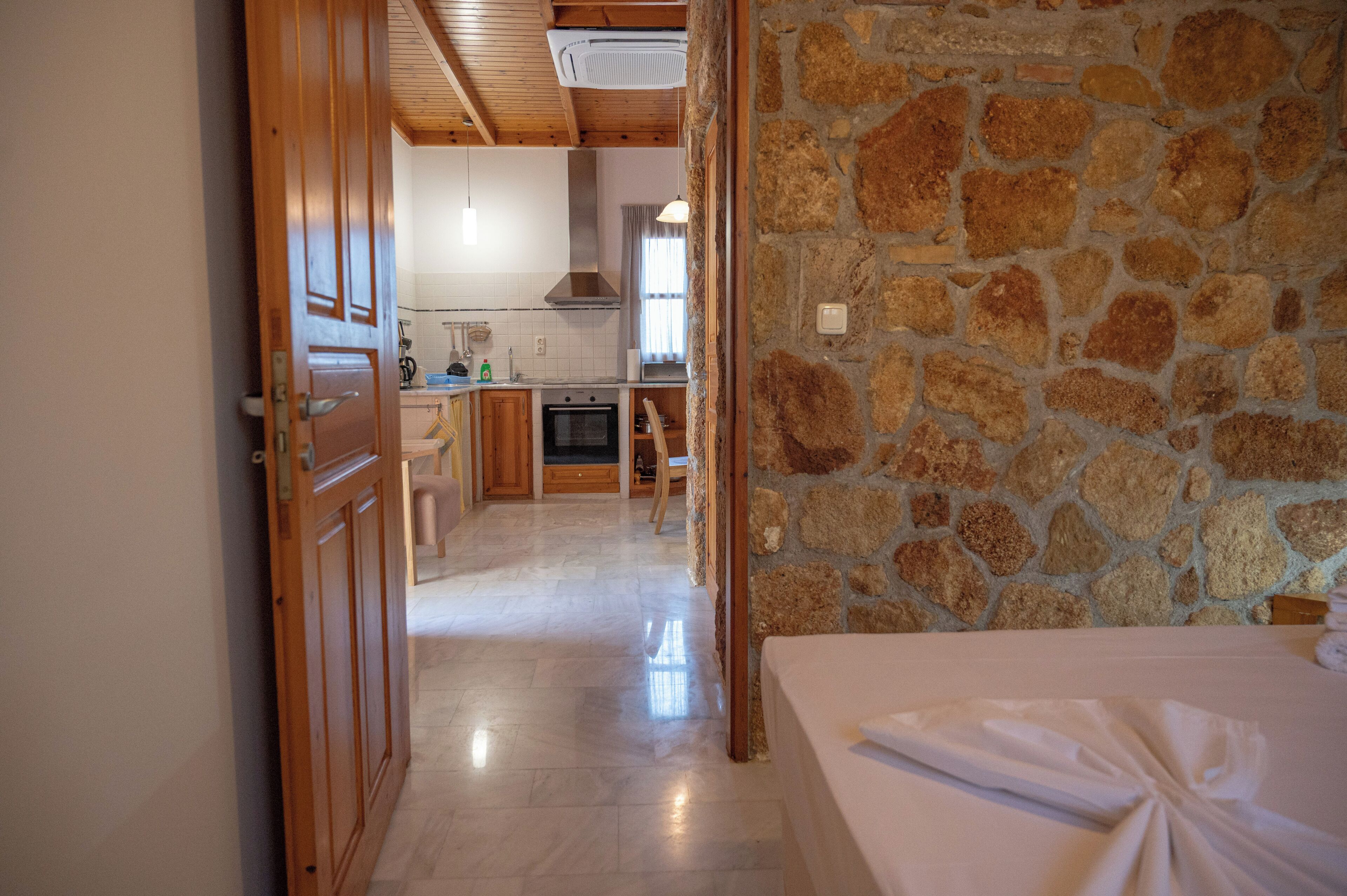 Une pièce avec un mur en pierre, un lit et une vue sur une cuisine dotée de meubles en bois et d’un plan de travail en pierre.