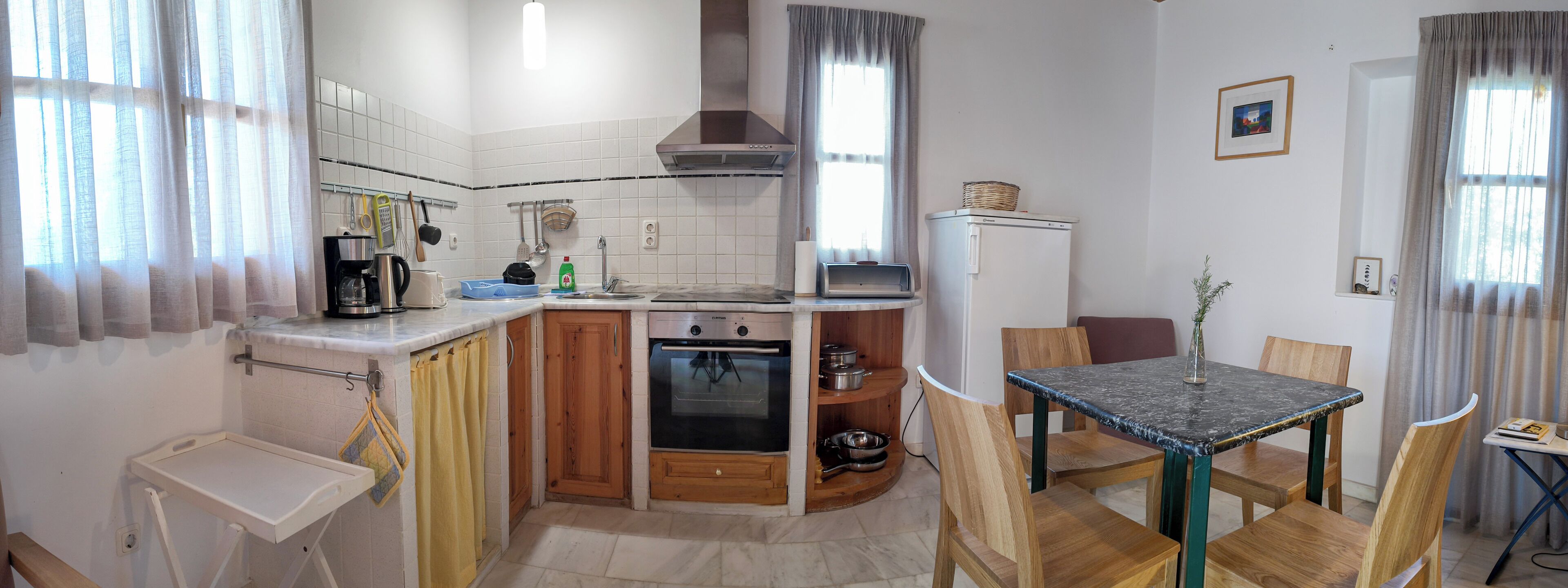 A compact kitchen with a built-in oven, a coffee maker, and a sink. There is a dining area with a table and chairs.