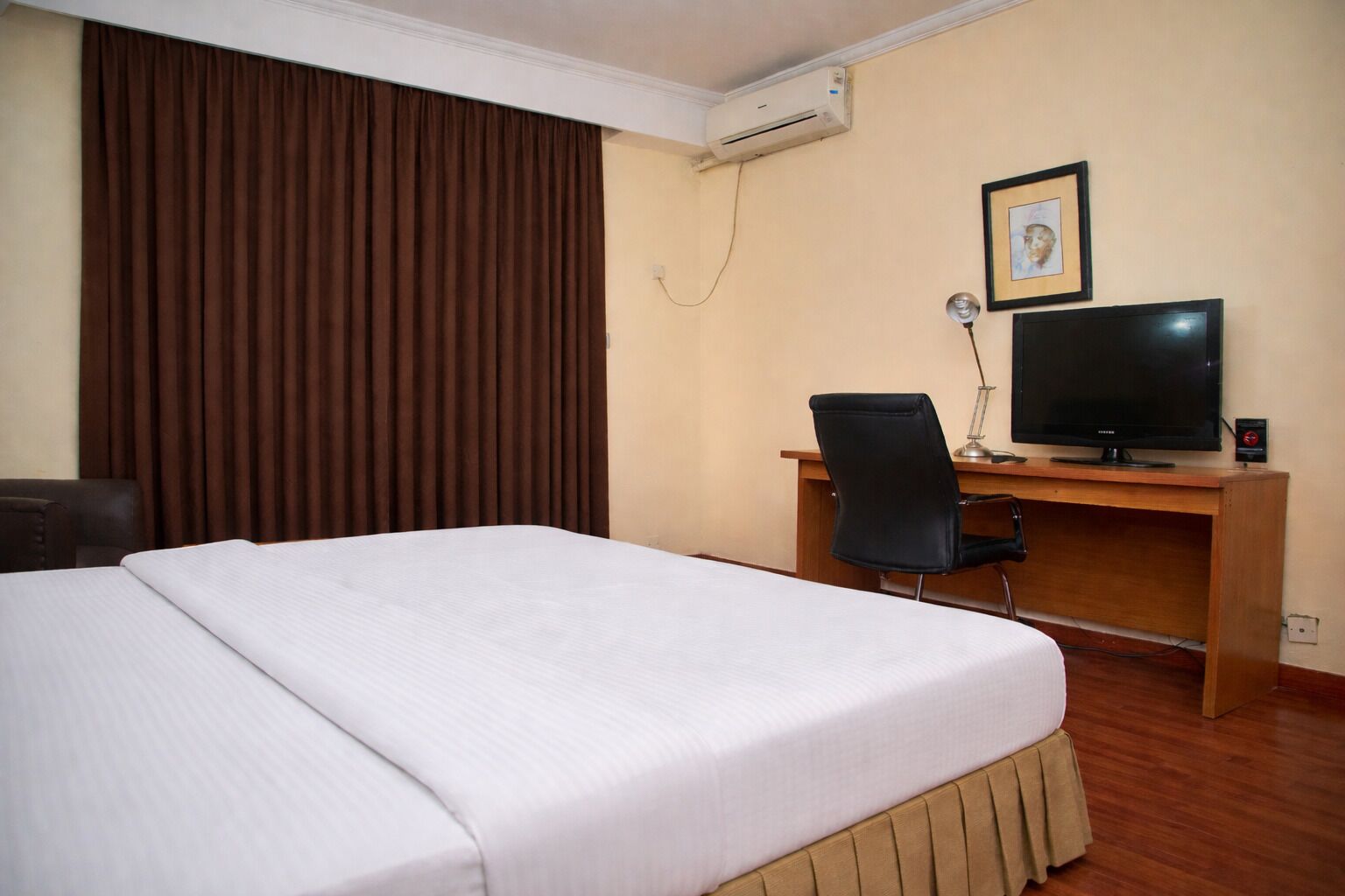 Habitación de hotel con cama, escritorio, silla, televisor y aire acondicionado.