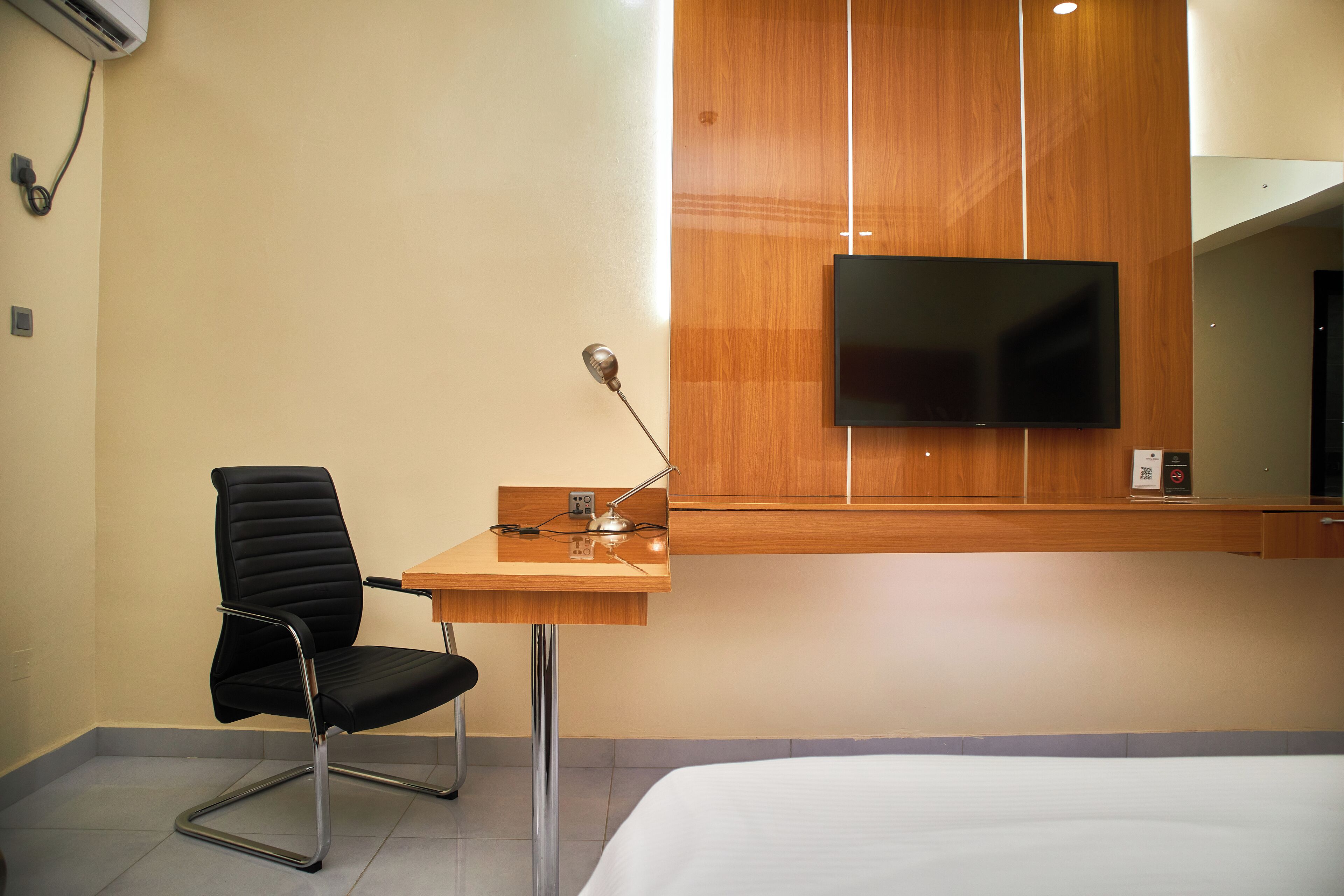 Ein Hotelzimmer mit Bett, Schreibtisch mit Stuhl, Flachbildfernseher an der Wand und einer Holzpaneelverkleidung.