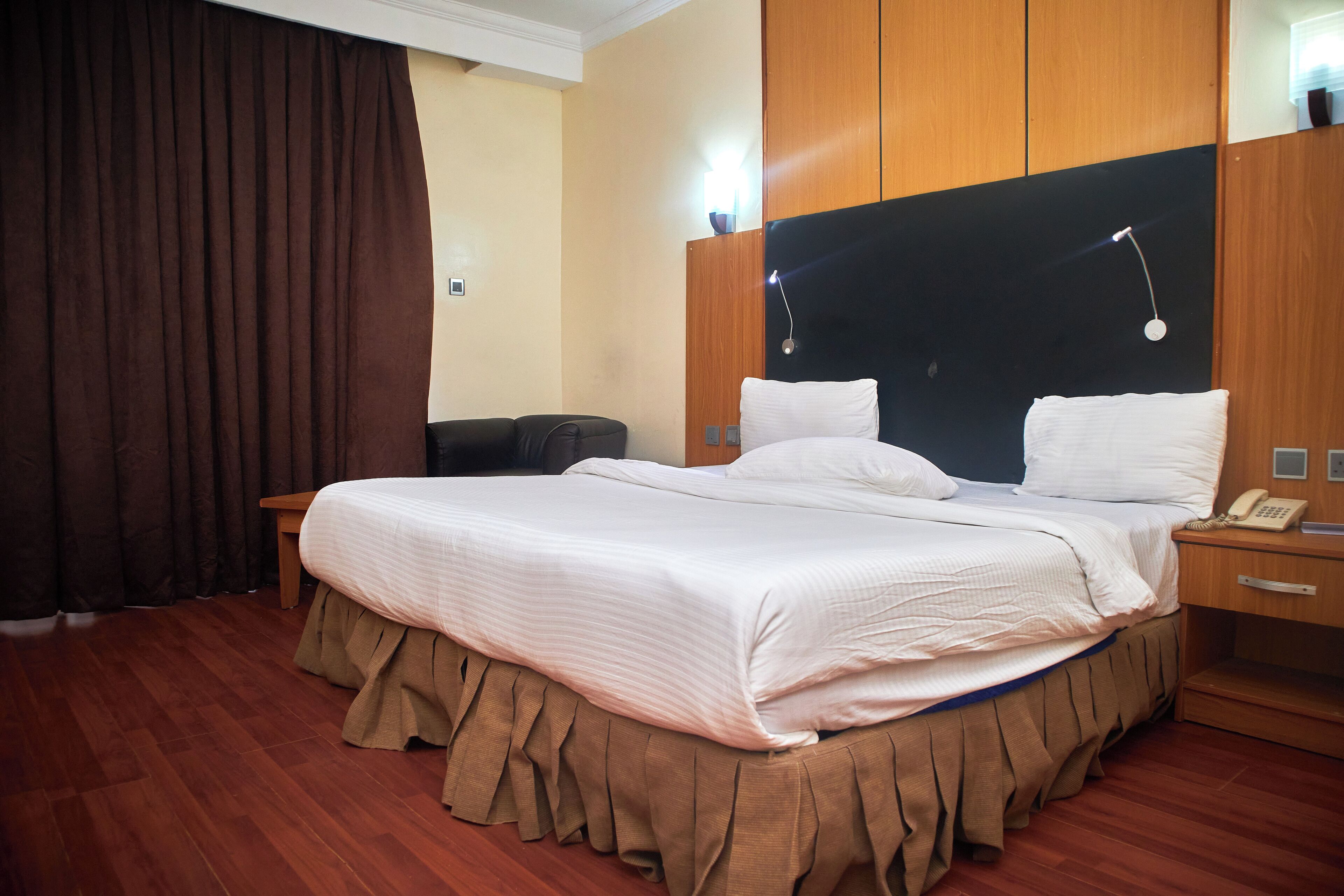 A hotel room with a large bed, a bedside table with a lamp, a wooden headboard, and a telephone.