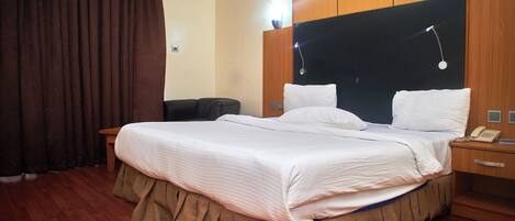 A hotel room with a large bed, a bedside table with a lamp, a wooden headboard, and a telephone.
