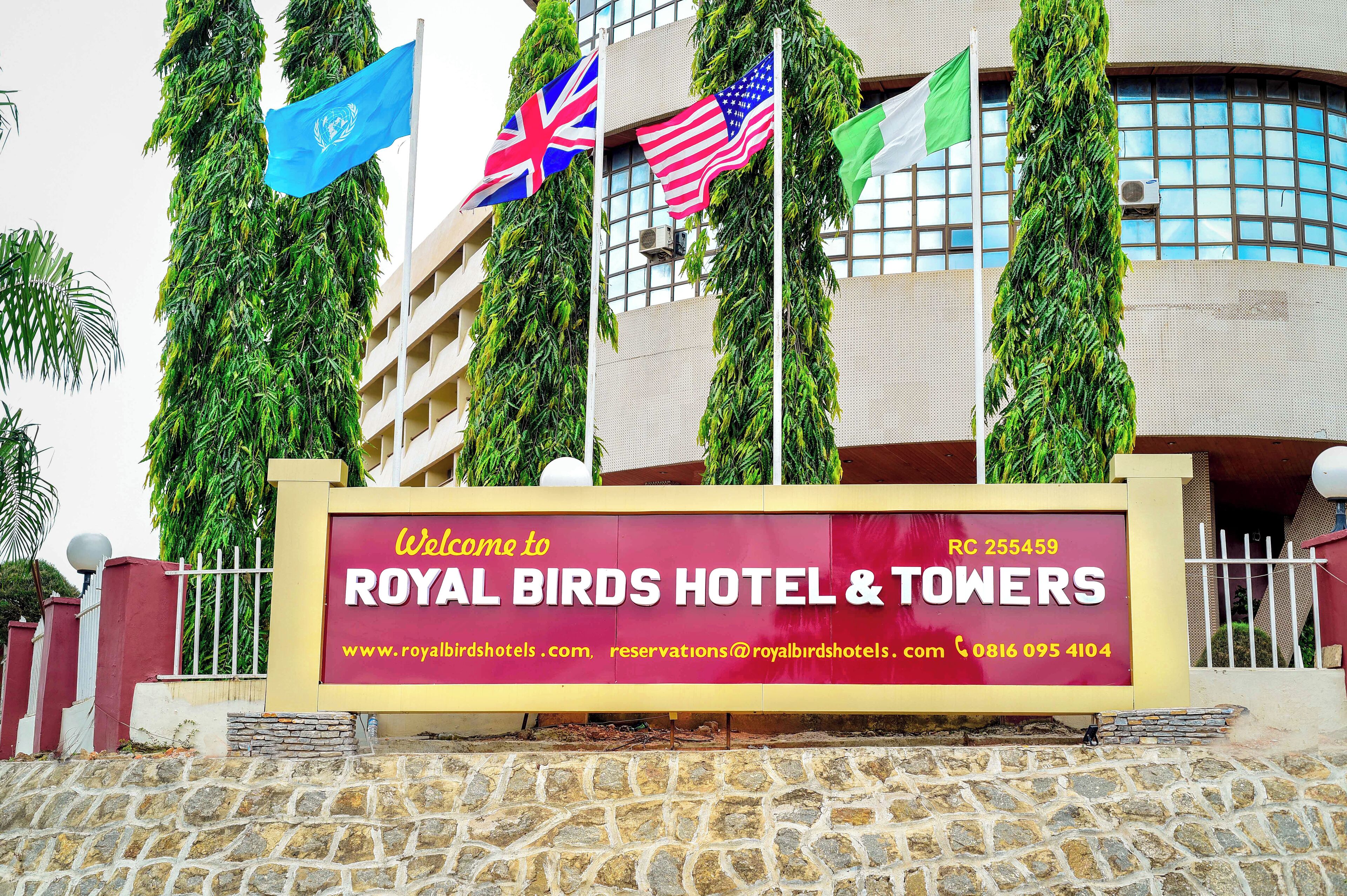 A hotel sign with flags, including the UN, UK, and US flags, and a welcome sign for Royal Birds Hotel & Towers.
