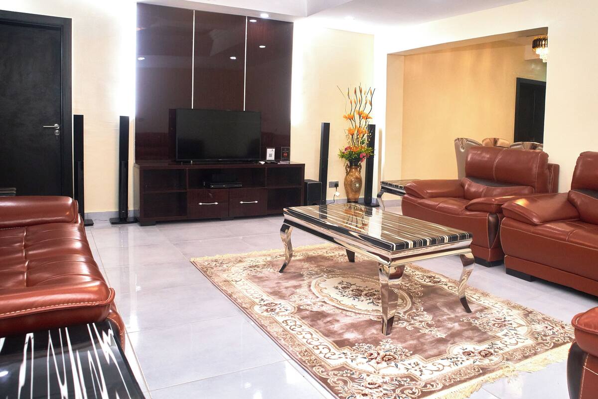 Uma sala de estar com televisão, sofás de couro, um tapete estampado e um vaso decorativo.
