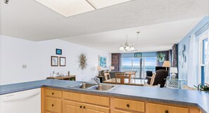 Une cuisine dotée d’un grand îlot central, d’un coin repas avec des chaises, d’une vue sur l’extérieur grâce à une porte vitrée et d’un ventilateur de plafond.