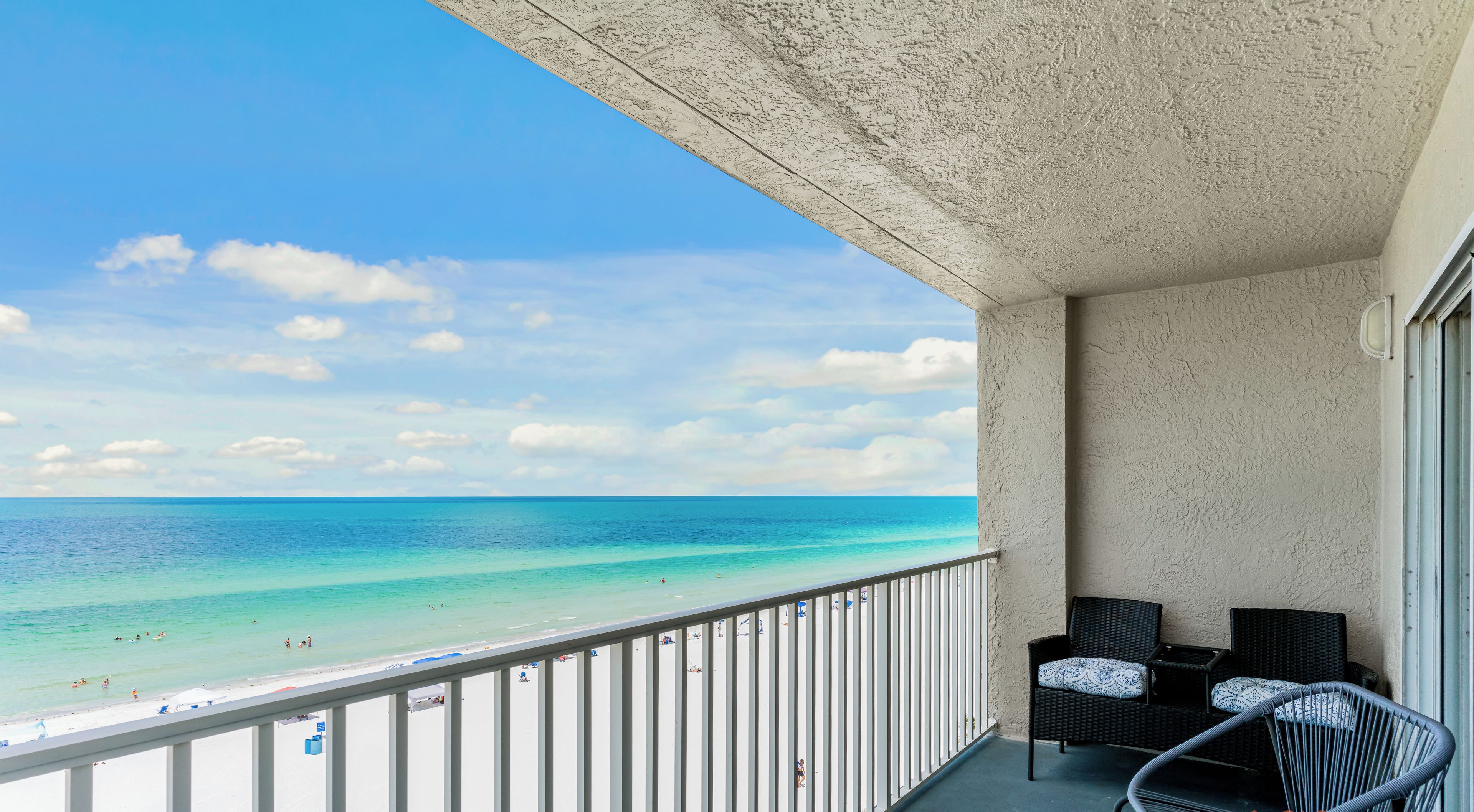 Un balcon avec vue sur la plage et l’océan. On y trouve deux fauteuils en osier avec des coussins.