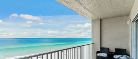 Un balcon avec vue sur la plage et l’océan. On y trouve deux fauteuils en osier avec des coussins.