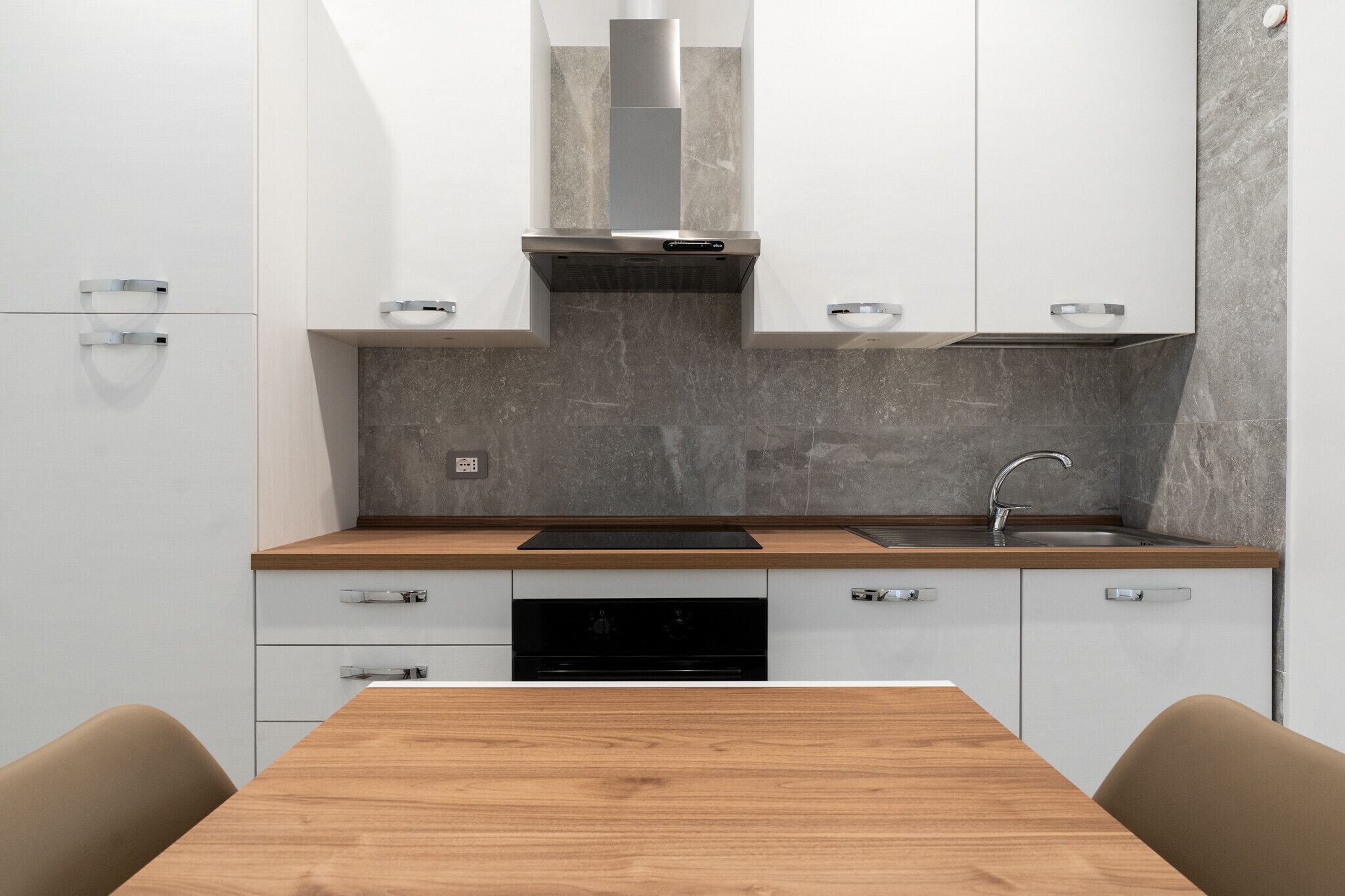 A modern kitchen with white cabinets, a wooden countertop, a stainless steel range hood, and a built-in dishwasher.