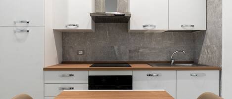 A modern kitchen with white cabinets, a wooden countertop, a stainless steel range hood, and a built-in dishwasher.