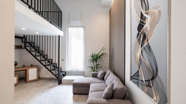 A modern living room with a staircase, a sectional sofa, a potted plant, and abstract art on the wall. - The Urban Nest Comfort Suite by Wonderful Italy (Bari)