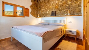 Un dormitorio con pared de piedra, una cama, una mesita de noche y una ventana con contraventanas de madera.
