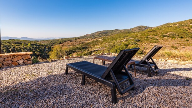 Dos sillones de relax sobre un terreno de grava con vistas a un paisaje montañoso.