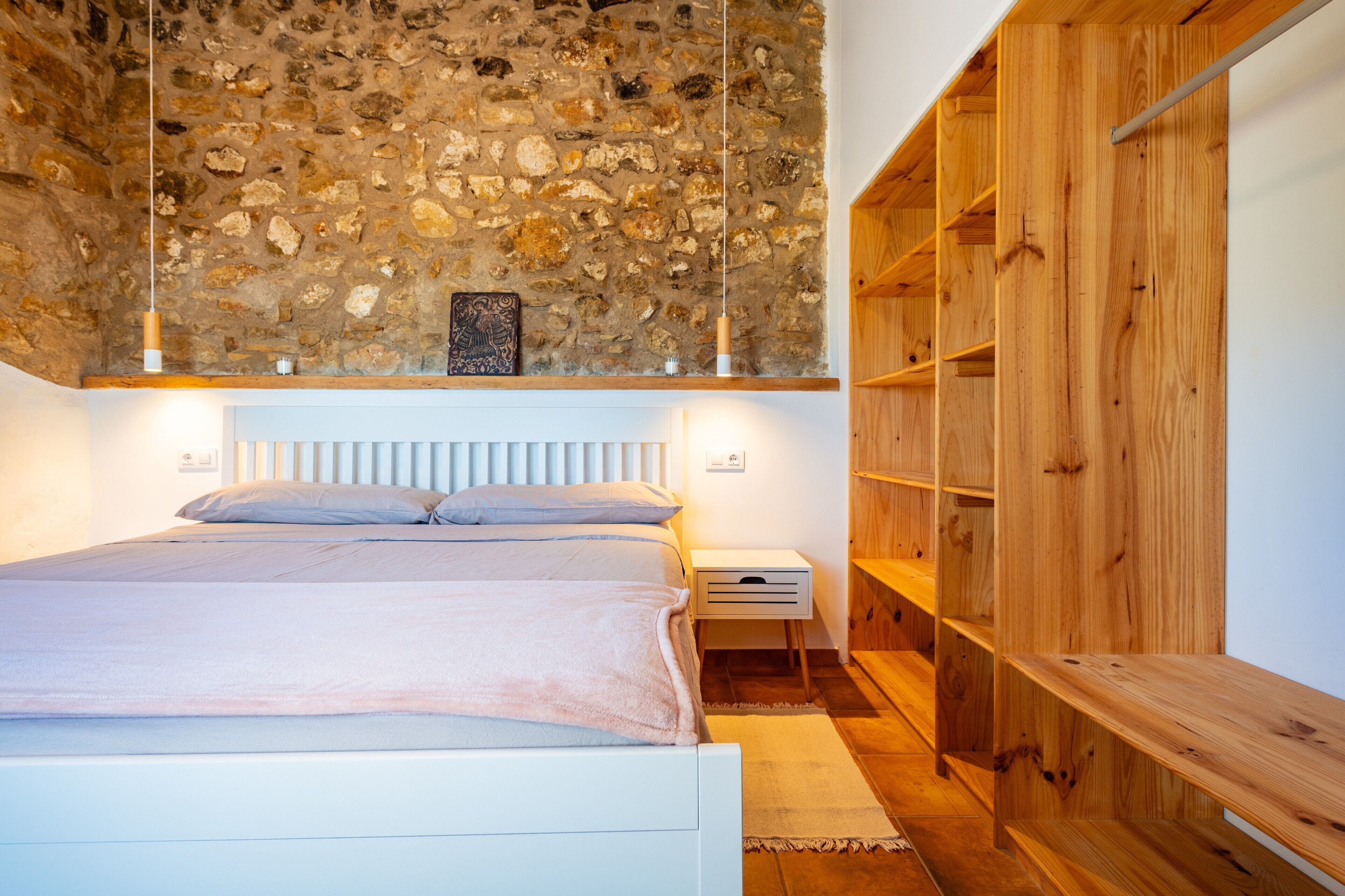 A bedroom with a stone ceiling, a bed with a white headboard, wooden shelves, and a nightstand.