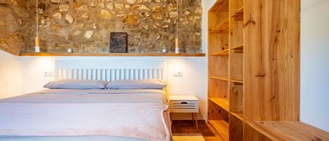 A bedroom with a stone ceiling, a bed with a white headboard, wooden shelves, and a nightstand.