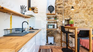 Una cocina con encimera de madera, un fregadero, microondas, cubo de basura, pared de piedra y un pequeño comedor con mesa y sillas.