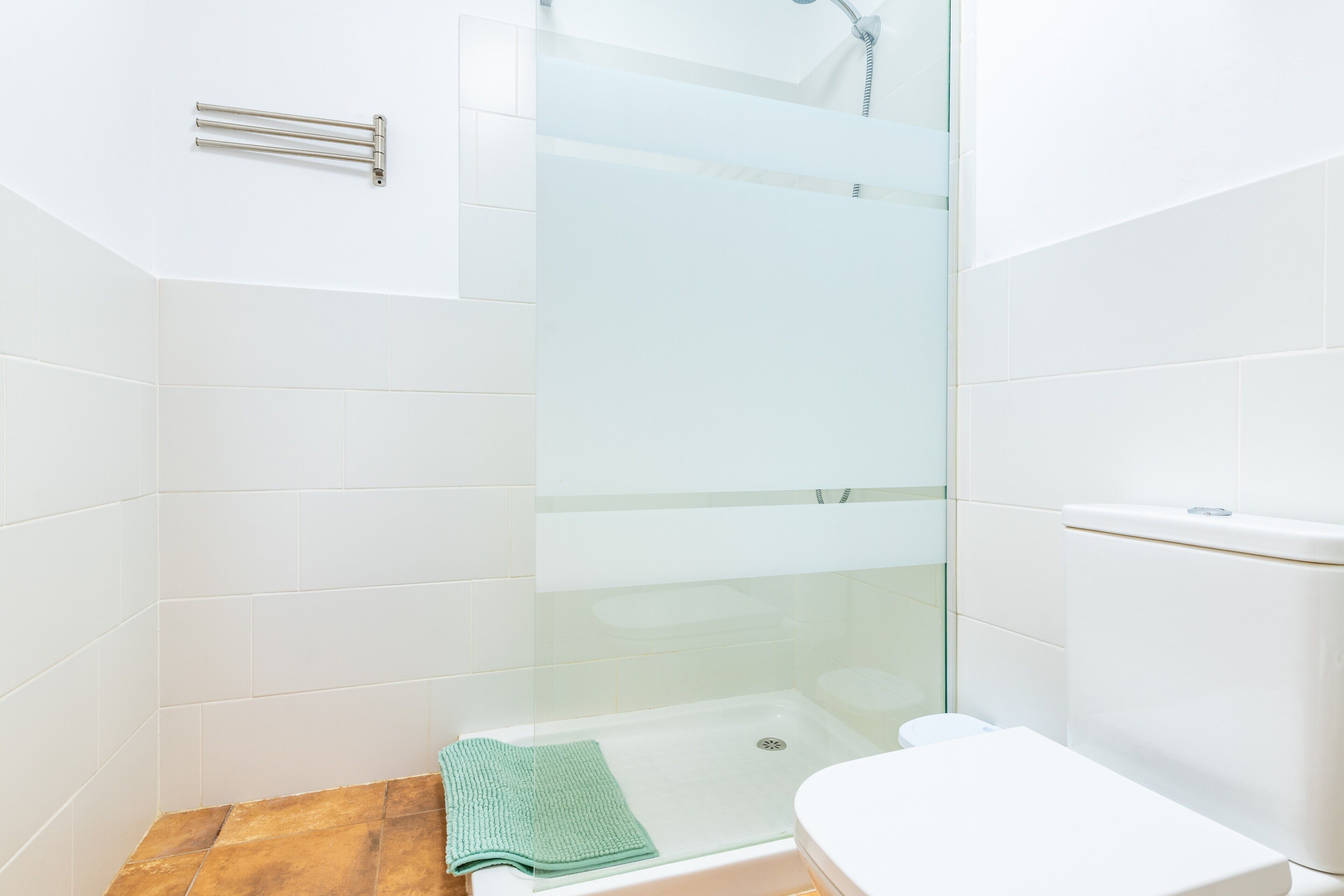 A bathroom with a glass-enclosed shower, a white toilet, and a towel on the floor.