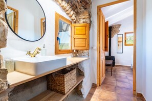 A bathroom with a white sink, wooden cabinets, a mirror, and stone walls.