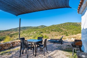 An outdoor patio with a table and chairs, a barbecue grill, and a view of green hills.