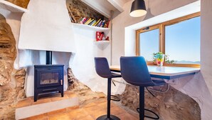 Un interior rústico con pared de piedra, chimenea, estantería y ventana con vistas.