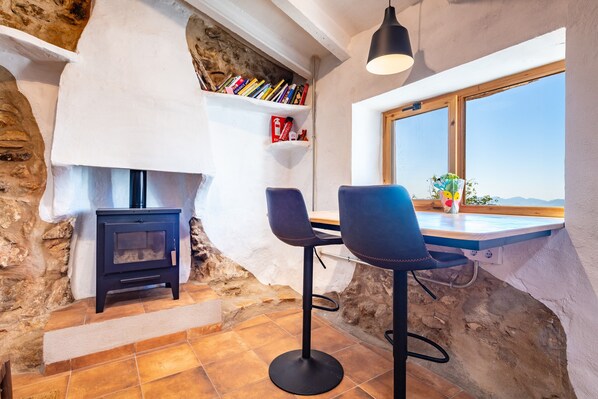 A rustic interior with a stone wall, a fireplace, a bookshelf, and a window with a view.