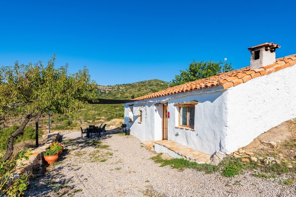 A white building with a tiled roof, a gravel path, and a small table and chairs outside.