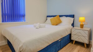 A neatly made bed with white and blue bedding, a yellow pillow, and a bedside lamp on a nightstand.